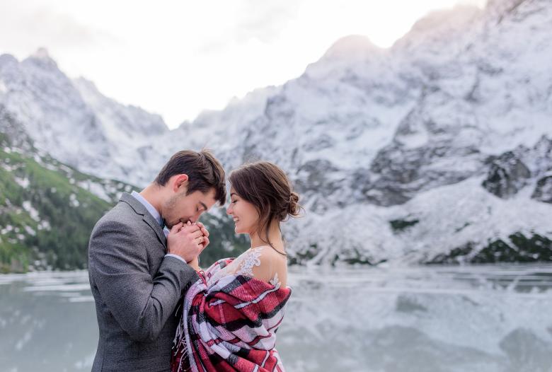 Groom kissing bride's hand in front of frozen lake 